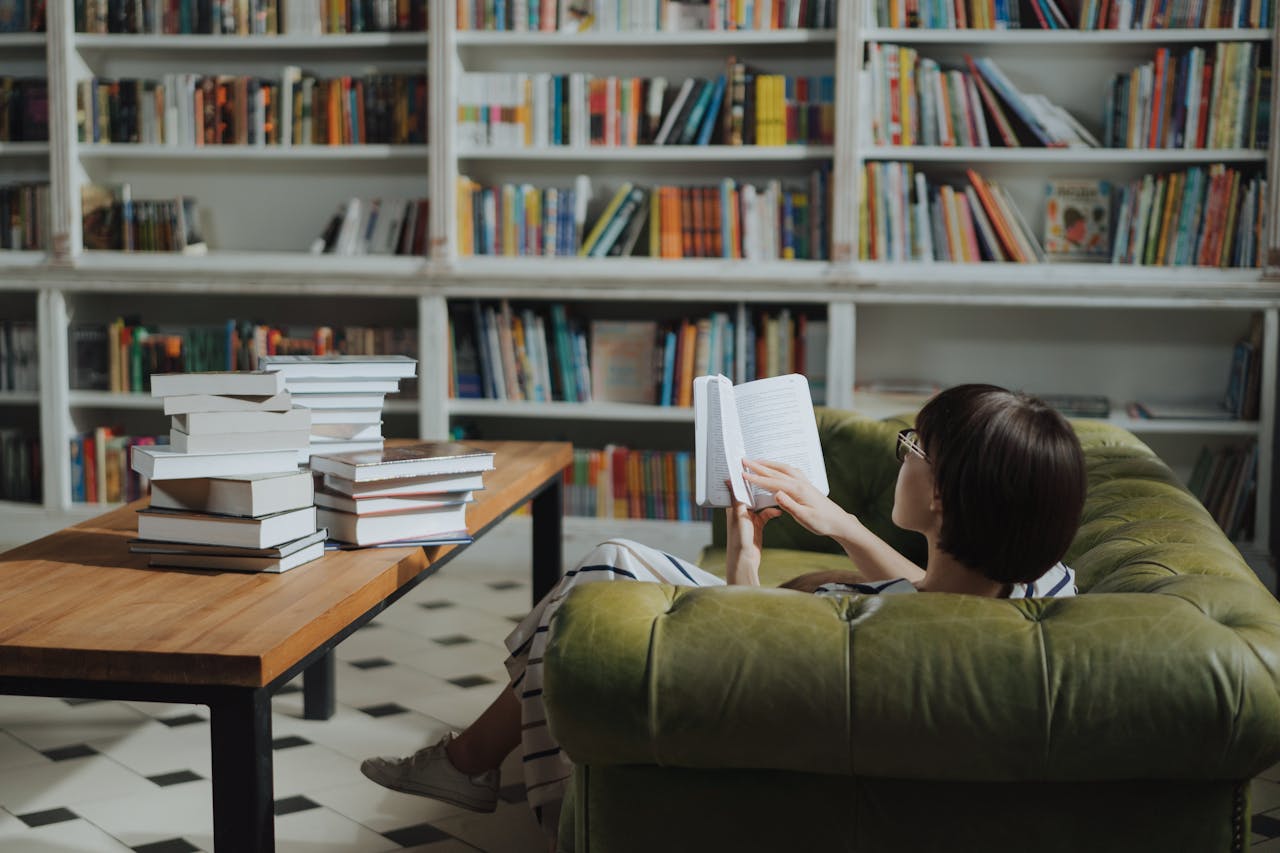 Woman reading on a sofa in a cozy library surrounded by book stacks.